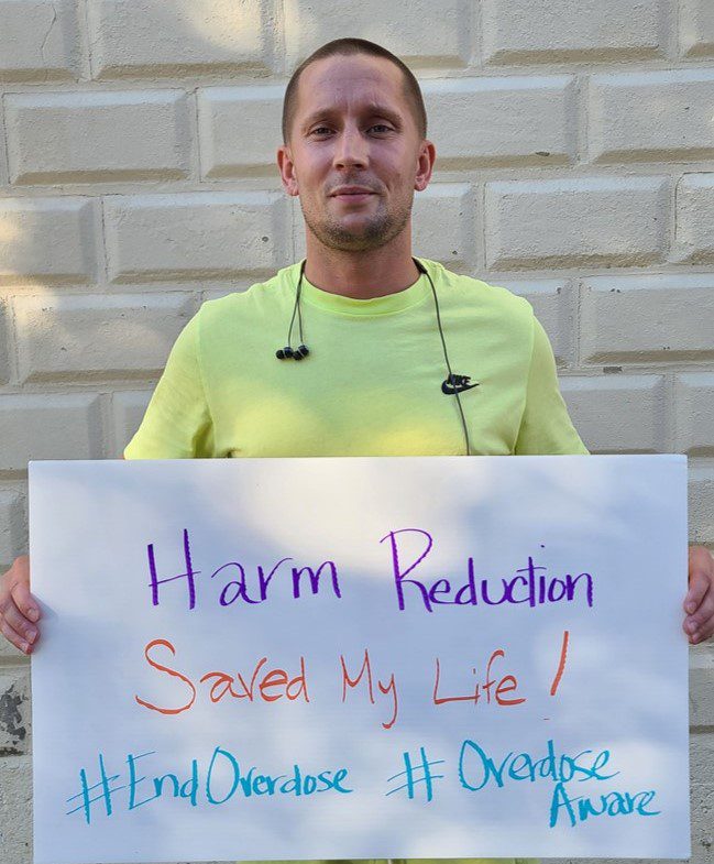 Ryan Harm Reduction group of men on porch holding we are recovering sign